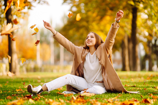 Young woman in park on sunny autumn day, smiling, having fun with leaves. Autumn fashion. Lifestyle. Relax, nature concept
