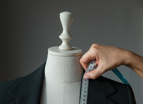 Woman measuring jacket on tailor mannequin.