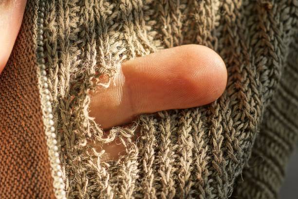 one brown finger in a hole in torn gray woolen fabric