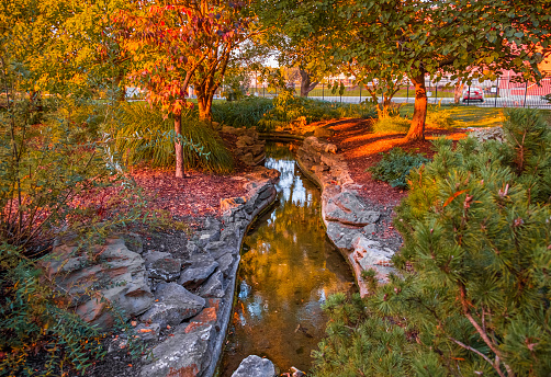 View of landscaped stream in Midwestern park at sunset in fall;