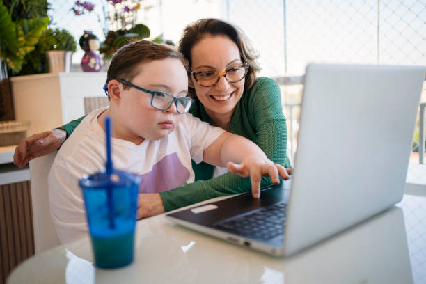 Mother helping son with down syndrome in homeschooling. Distance learning concept. stock photo