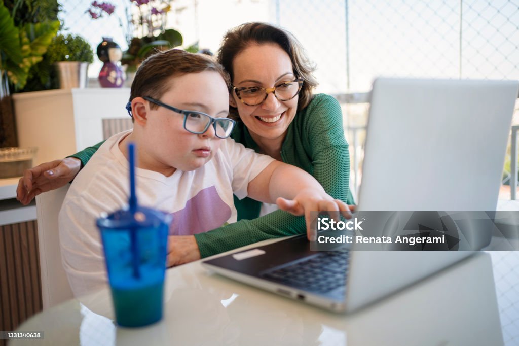 Mother helping son with down syndrome in homeschooling. Distance learning concept. - Royaltyfri Funktionsnedsättning Bildbanksbilder