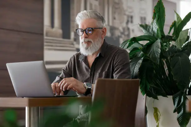 an incredibly beautiful and stylish gray-haired man of fifty years old working with a laptop, a European business man is a director or a top manager in an office or in a VIP airport waiting room, a handsome man is an entrepreneur, an engineer or an