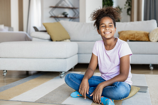 African American teenage girl at home, sitting on the floor and smiling