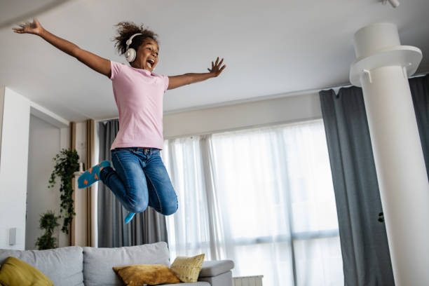 音楽を聴きながらソファジャンプをしている幸せな女の子 - domestic life jumping child sofa ストックフォトと画像