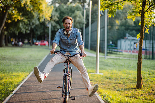 A young cheerful man riding a bike in a park