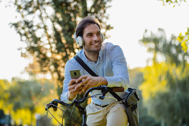 istock Young man on a bicycle using mobile phone after work and headphones 1331344999