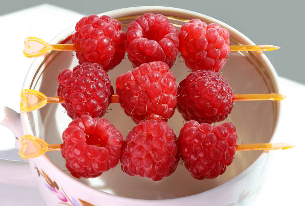 Red raspberry berries, pierced on canapes on edge of cup, close-up
