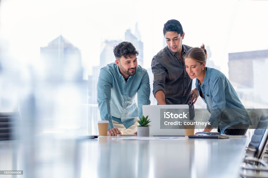 Business team working on a laptop computer. Business team working on a laptop computer. Three people are wearing  casual clothing. They are standing in a board room. Multi ethnic group with Caucasian and Latino men and women Office Stock Photo