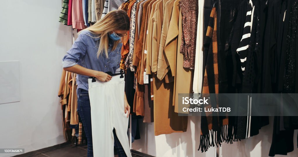 Shopping habits die hard A look at a young woman that is shopping during the Covid-19 pandemic. She's looking at fancy pants she took from the rack. 20-24 Years Stock Photo