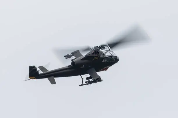 The shape of an AH-1 Cobra attack helicopter (in Vietnam war color scheme, with shark teeth)  against the sky, with rockets and machine gun