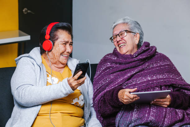 mujeres latinas de la tercera edad escuchando música con auriculares en casa en la ciudad de méxico, gente mexicana - senior couple audio fotografías e imágenes de stock