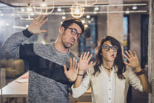 istock Young playful entrepreneurs making faces while playing with glass wall. 1331396352