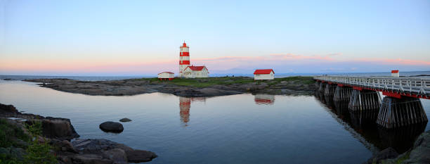 Panoramic view of Pointe-des-Monts Lighthouse at sunset with reflections in the sea, Cote-Nord, Quebec Panoramic view of Pointe-des-Monts Lighthouse at sunset with reflections in the sea, Cote-Nord, Quebec cote nord photos stock pictures, royalty-free photos & images