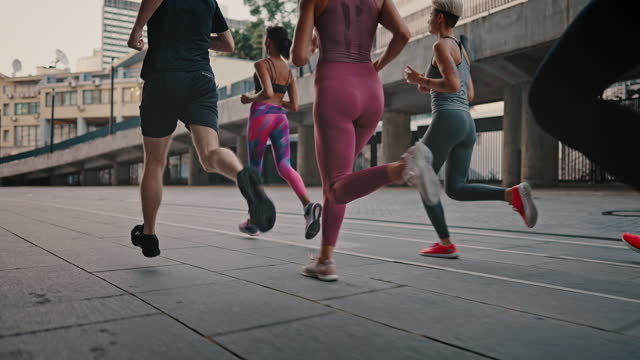 Close-up of legs of athletes in sports shoes. Rear view athletes runners train in the stadium. Young team of man and woman in sportswear. Like-minded club