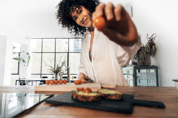 istock Woman preparing breakfast showing a tomato looking at camera in bright loft kitchen. Selective focus on face. 1331412489