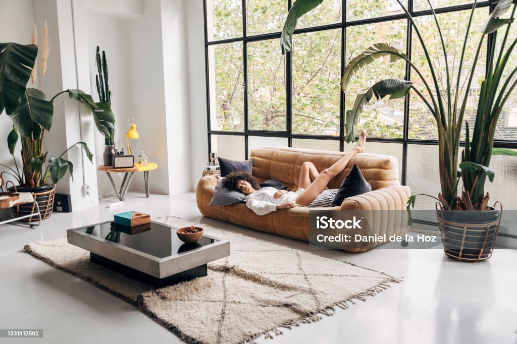 Beautiful and young african american woman sleeping on a couch in a big bright living room. Copy space Beautiful and young african american woman sleeping on a couch in a big bright living room. Home concept. Copy space Living Room Stock Photo