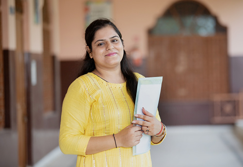 Confident smiling Indian school teacher with students in background