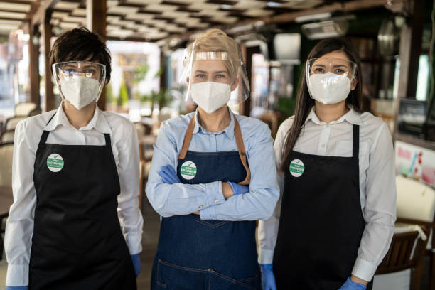 istock Restaurant owner and waitresses working at a restaurant, wearing a double protective face masks and a badge showing that they are vaccinated against COVID-19. 1331430897