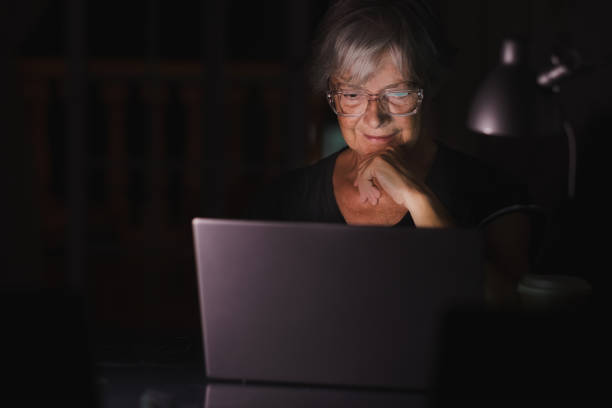 istock Senior woman looking and using laptop at home late night working watching videos on computer 1331431305