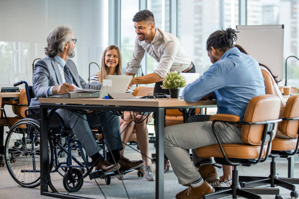 Selective focus of smiling disabled businessman and colleagues in office. Selective focus of smiling disabled businessman and colleagues in office. Side View Of A Disabled Businessman. Young businessman greeting handicapped business partner and team. Coworker on wheelchair place of work stock pictures, royalty-free photos & images