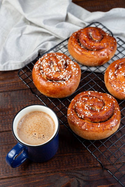Freshly baked traditional Swedish cinnamon buns Kanelbulle with cup of coffee or cappuccino, on wooden background, vertical Freshly baked traditional Swedish cinnamon buns Kanelbulle with cup of coffee or cappuccino, on a wooden background, vertical kanelbulle stock pictures, royalty-free photos & images