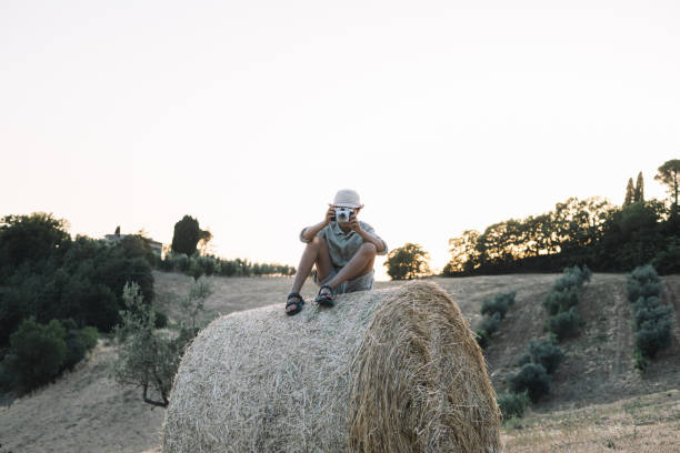 Girl takes pictures with her camera, sitting on a roll of straw