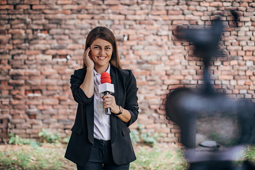 One woman, female television reporter talking on microphone outdoors by a brick wall.She is checking hearing from the studio
