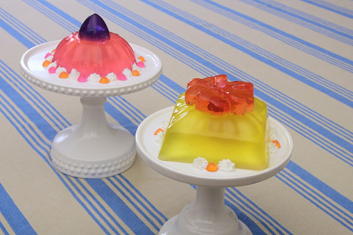 A modern spin on retro jello desserts - ornate, colorful and fanciful tiered molded gelatin decorated with cream displayed on cake stands.