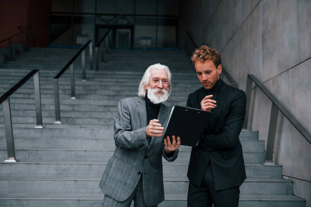 istock Holding notepad. Young guy with senior man in elegant clothes is outdoors together. Conception of business 1331446563