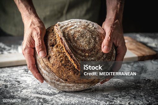 istock Male hands holding Sourdough bread brown round loaf wholegrain homemade German style 1331448579