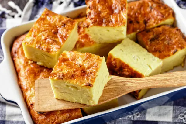 potato kugel, baked pudding or casserole of grated potato cut in portions in a baking dish on a wooden table, jewish holiday recipe, close-up