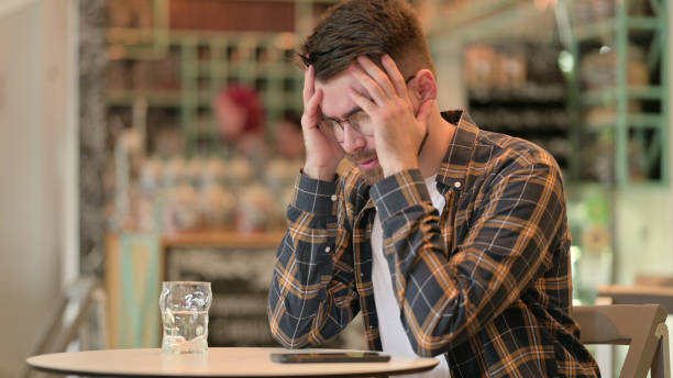 istock Worried Young Man with Headache sitting in Cafe 1331453898