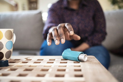 Girl suffering asthma attack reaching inhaler sitting on a couch in the living room at home