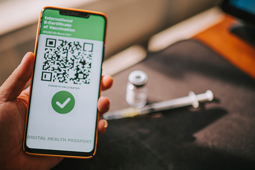 asian chinesa man holding smart phone device screen on vaccination passport mobile app above coronavirus vaccine bottle and syringe injection