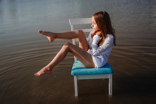 A beautiful small girl in a chair in the middle of a pond. The idea and concept of freedom and loneliness