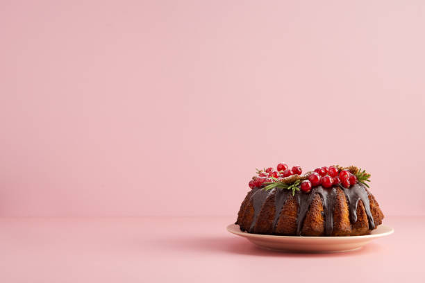 tort bożonarodzeniowy na różowym tle. przestrzeń do kopiowania w poziomie dla tekstu. ciasto z czekoladową glazurą i jagodami z czerwonej porzeczki - christmas cake zdjęcia i obrazy z banku zdjęć