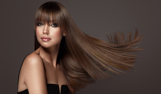 Attractive young woman with chubby, well shaped lips and green eyes with smoky eyeshadows makeup is demonstrating long, straight, dense hairstyle with long, straight fringe.Flying hair.