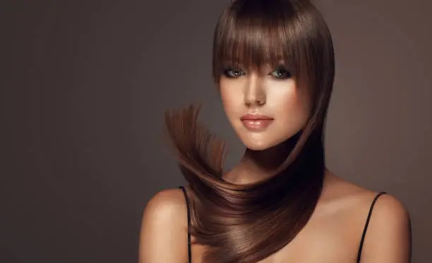 Elegant splash of brown hair around attractive face of young woman.Long, straight, dense hairstyle with long, straight fringe. Flying hair. Hair care and hairdressing art.
