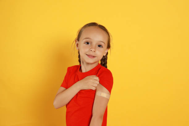 黄色の背景に対して彼女の腕に医療石膏を示す予防接種を受けた小さな女の子 - little girls vaccination child caucasian ストックフォトと画像