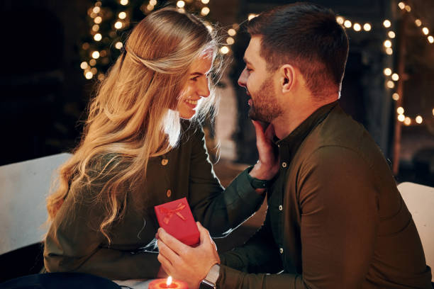 istock Man holds gift box. Makes proposal mo marry him. Young lovely couple have romantic dinner indoors together 1331468558