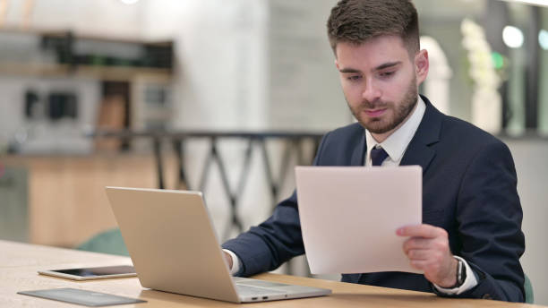 istock Serious Businessman working on Laptop with Documents in Office 1331470047