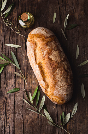 Artisan white baked bread on the wooden rustic background  with olive branches and olive oil, rustic style, basic organic ingredient