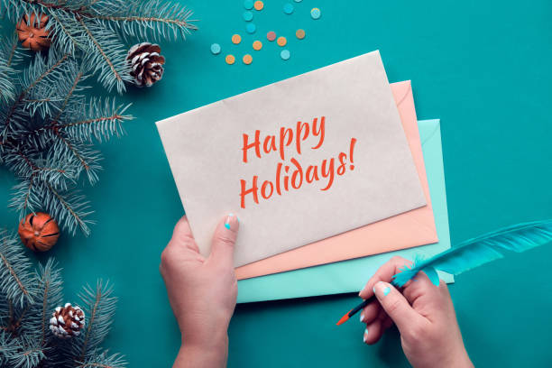 istock Traditional Christmas background with text Happy Holidays on postcards. Hands with greeting cards and quill. Top view on fir twigs decorated with red glass baubles, Xmas toys. Paper confetti 1331473637