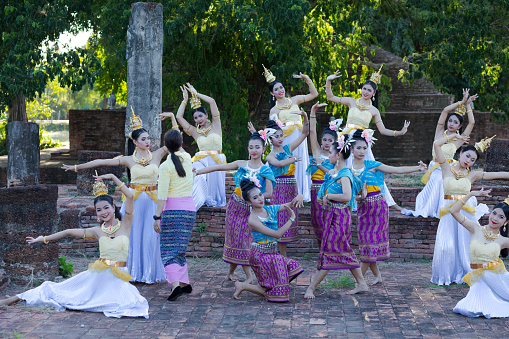 Rum Thai dance performance scene at temple ruins in Phitsanulok. Young dancers in period costumes are performing and exercising for evening history event at temple. 2019 was historical event at and around temple ruin Wat Wihan Thong Historical Site with food market and dance shows events for publicity and admission free. Typical thai true classic market and event festival