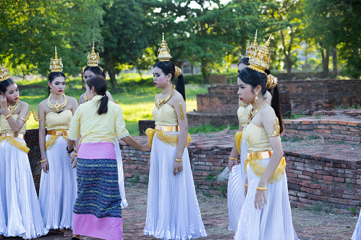 Young female thai dancers are listening teacher and instructions for rum thai performance. Dancers are wearing period costumes and gold colored crowns. Scene is at temple ruin in Phitsanulok and they are exercising for evening history dance show. 2019 was historical event at and around temple ruin Wat Wihan Thong Historical Site with food market and dance shows events for publicity and admission free. Typical thai true classic market and event festival