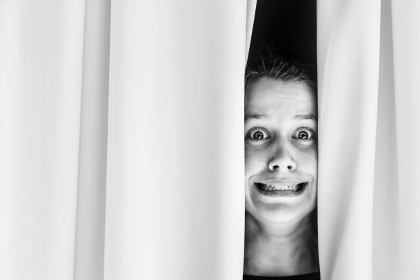 istock Terrified young woman grimaces as she sees something shocking through her curtains 1331486864