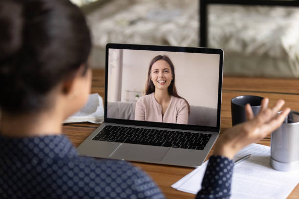 Happy young millennial colleagues having virtual talk Happy young millennial colleagues having virtual talk, discussing work project. Teacher training student via video call. Women teaching and studying language online. Screen display view over shoulder interview stock pictures, royalty-free photos & images