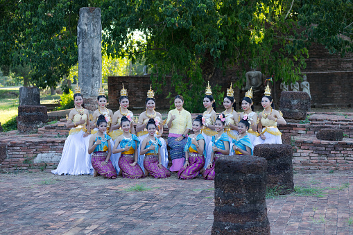 Group arrangement of thai dancers with teacher in ruins of temple in Phitsanulok. Group has finished exercise for evening event. They are sitting for a person of group out of sight for photos. 2019 was historical event at and around temple ruin Wat Wihan Thong Historical Site with food market and dance shows events for publicity and admission free. Typical thai true classic market and event festival