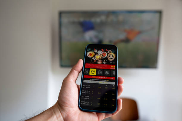 Man watching a football match and gambling on a mobile app Man watching a football match and gambling on a mobile app - sports betting concepts. **DESIGN ON BOTH SCREENS WERE MADE FROM SCRATCH BY US** sports betting stock pictures, royalty-free photos & images